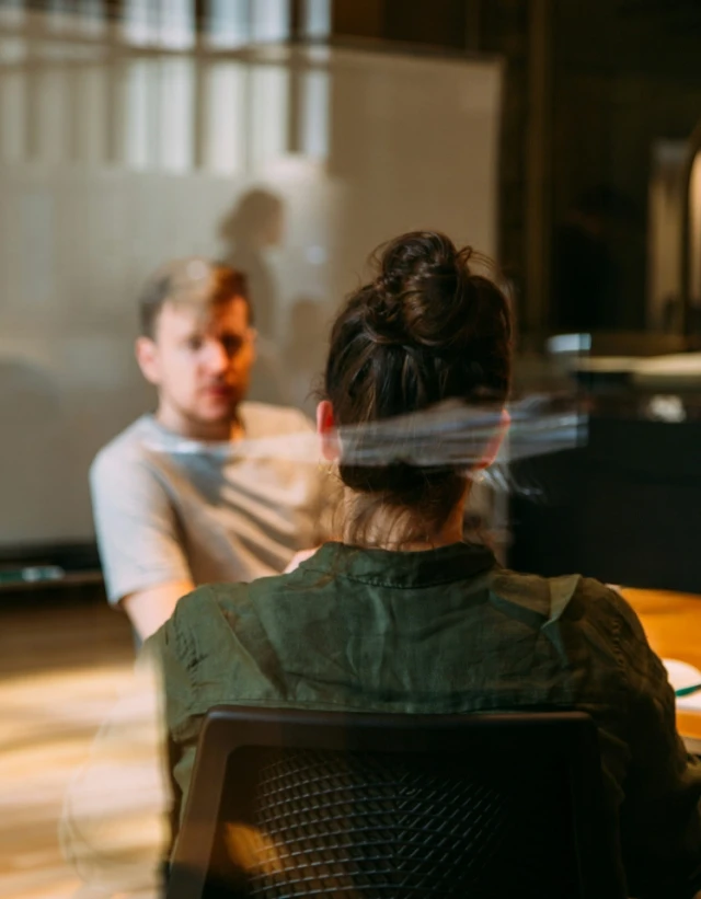 A founder in conversation across a table, seen through glass in low afternoon light